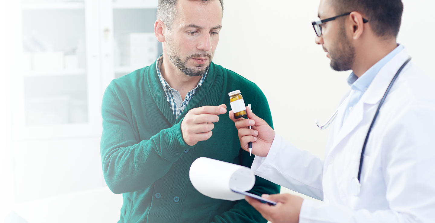 A doctor in a white coat hands a medication bottle to a concerned patient in a green sweater.