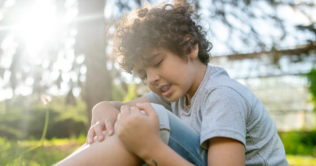 Child sitting outdoors and holding a painful knee.