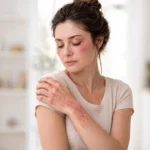 Woman looking down while holding her arm, showing red skin rash lesions on her arm and face.