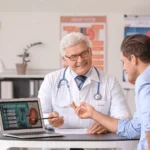 Male doctor pointing at a urology presentation on a laptop during a patient consultation.