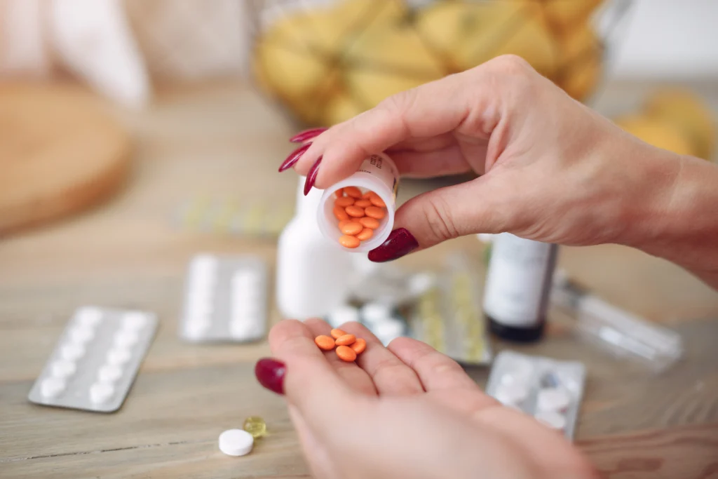 Close-up of a person pouring small round orange pills out of a bottle into their hand